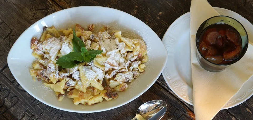 Kaiserschmarren auf einem weißen Teller, daneben Apfelkompott in einem Glas