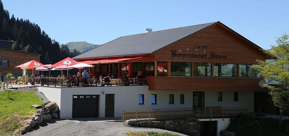 Das Haus und die Sonnenterrasse mit roten Schirmen, von der Zufahrt aus gesehen