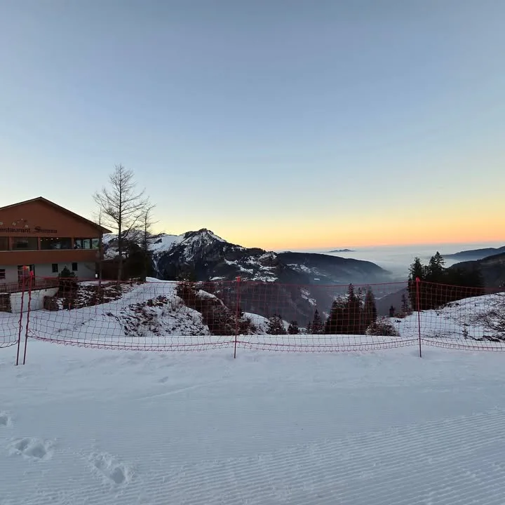 Das Haus im Winter bei Morgenrot, davor die frisch präparierte Piste