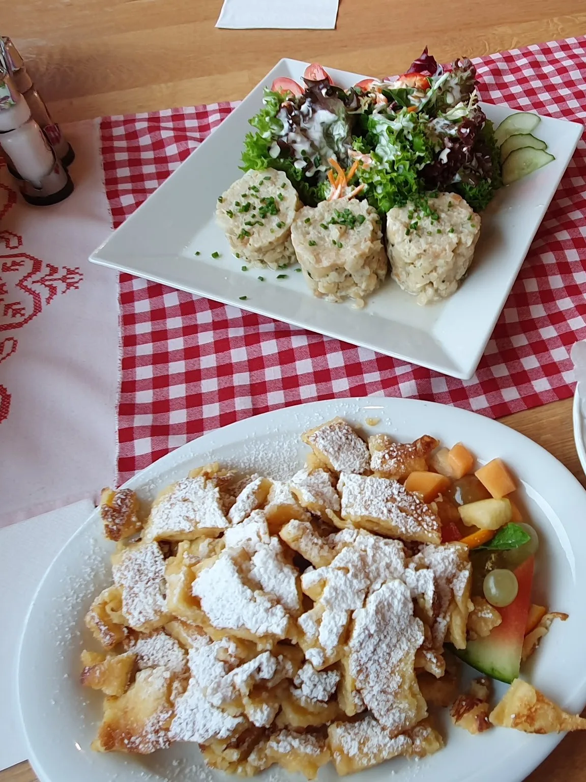 Gedeckter Tisch mit rot-weiß kariertem Läufer, ein Knödelgericht mit Salat und Kaiserschmarren mit Früchten