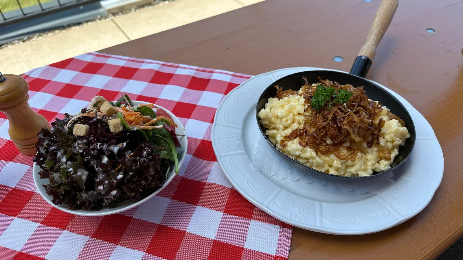 Bregenzerwälder Käsknöpfle in der Pfanne mit Röstzwiebeln, daneben ein Salatteller
