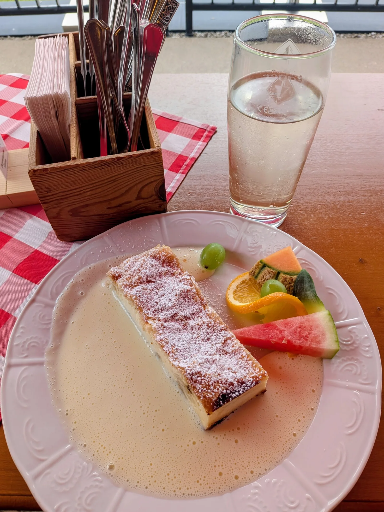 Ein Stück Strudel mit Vanillesauce auf einem Teller, daneben ein Besteckkorb